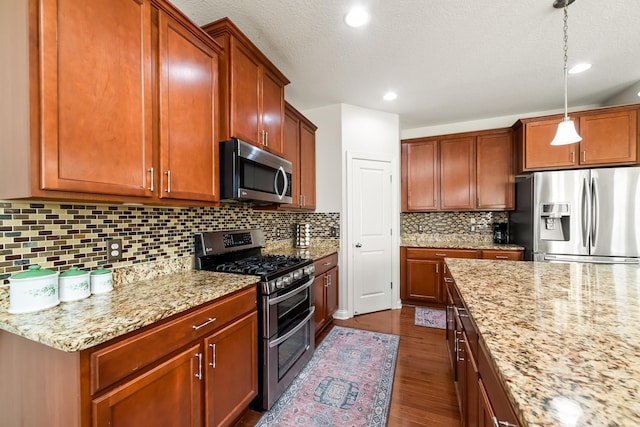 kitchen featuring hanging light fixtures, light stone counters, dark hardwood / wood-style floors, decorative backsplash, and appliances with stainless steel finishes