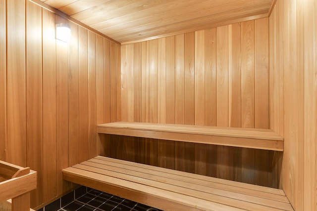 view of sauna / steam room with tile patterned flooring, wood ceiling, and wooden walls