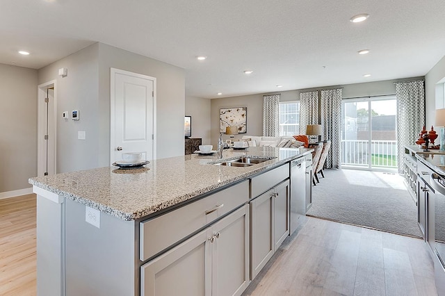 kitchen featuring an island with sink, light hardwood / wood-style flooring, gray cabinetry, sink, and light stone counters