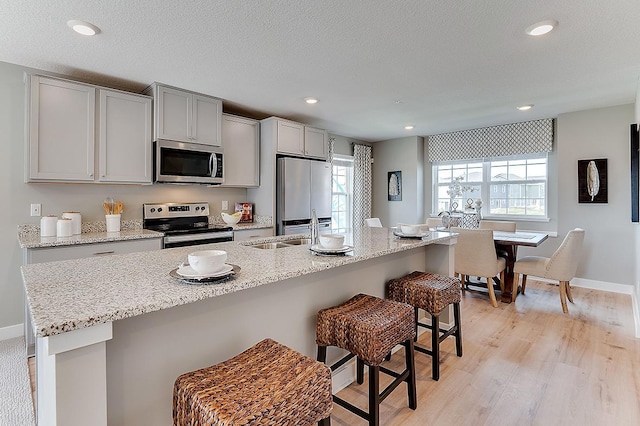 kitchen featuring a wealth of natural light, a kitchen breakfast bar, appliances with stainless steel finishes, and light hardwood / wood-style floors