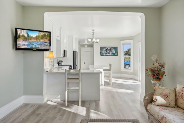 kitchen with appliances with stainless steel finishes, kitchen peninsula, a breakfast bar area, white cabinetry, and light hardwood / wood-style flooring