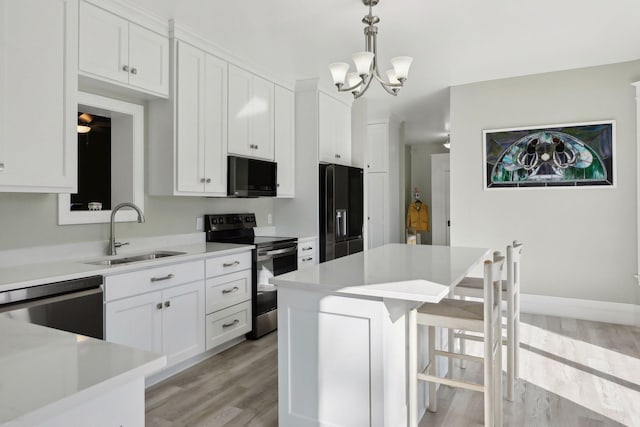 kitchen featuring white cabinets, black appliances, light hardwood / wood-style floors, decorative light fixtures, and sink