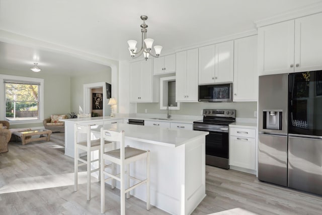 kitchen featuring stainless steel appliances, light hardwood / wood-style flooring, pendant lighting, and white cabinets