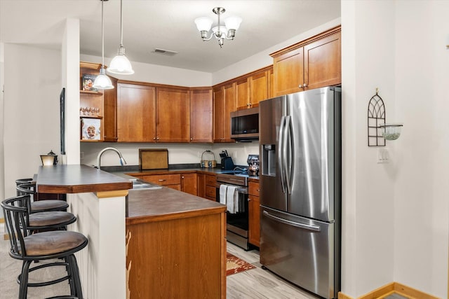 kitchen featuring appliances with stainless steel finishes, sink, kitchen peninsula, decorative light fixtures, and light hardwood / wood-style flooring