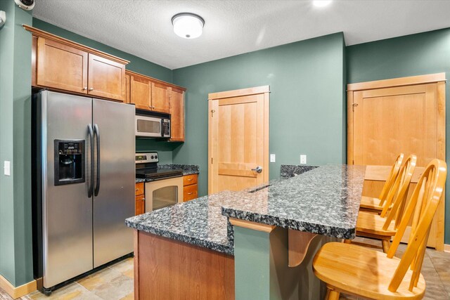 kitchen with kitchen peninsula, a kitchen breakfast bar, a textured ceiling, dark stone countertops, and stainless steel appliances