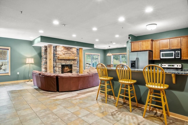 kitchen featuring a stone fireplace, stove, a kitchen bar, and stainless steel fridge with ice dispenser