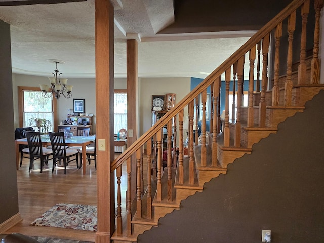 stairs featuring an inviting chandelier, wood finished floors, and a textured ceiling
