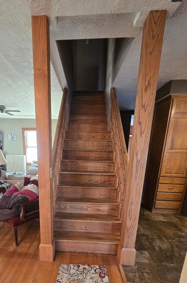 stairway featuring wood finished floors, a textured ceiling, and ceiling fan