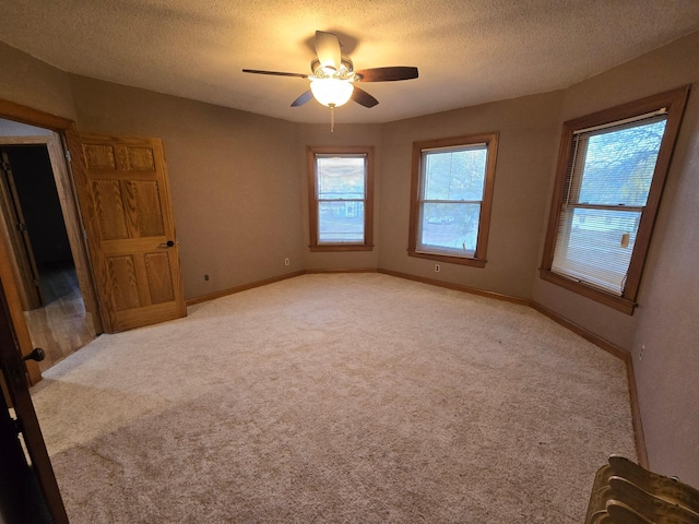 spare room with ceiling fan, light carpet, a textured ceiling, and baseboards
