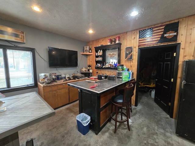 bar featuring recessed lighting, concrete flooring, wet bar, and freestanding refrigerator