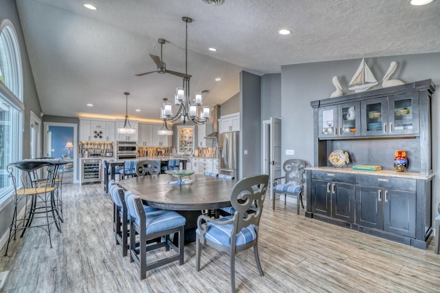 dining area featuring light wood-type flooring, beverage cooler, a textured ceiling, high vaulted ceiling, and ceiling fan