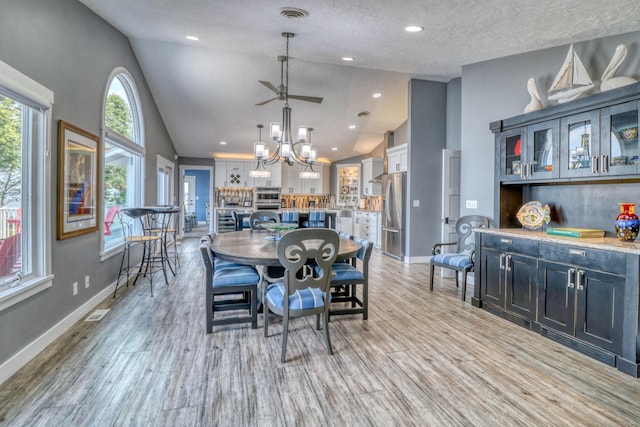 dining space featuring light hardwood / wood-style flooring, a textured ceiling, high vaulted ceiling, and ceiling fan with notable chandelier