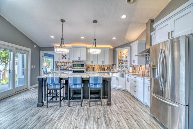 kitchen with lofted ceiling, a kitchen island, decorative light fixtures, appliances with stainless steel finishes, and light hardwood / wood-style floors