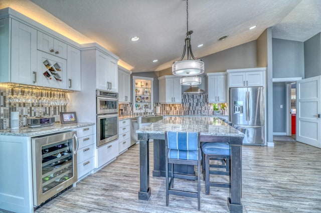 kitchen featuring light stone countertops, appliances with stainless steel finishes, vaulted ceiling, decorative light fixtures, and decorative backsplash