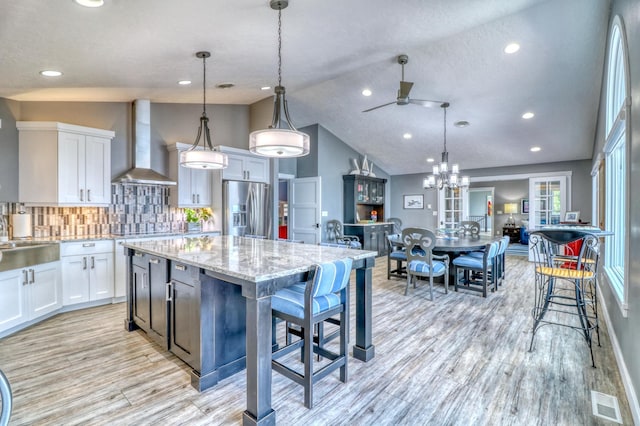 kitchen featuring appliances with stainless steel finishes, wall chimney range hood, decorative light fixtures, and white cabinets