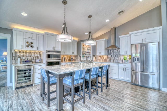 kitchen with light stone countertops, wall chimney range hood, stainless steel appliances, lofted ceiling, and beverage cooler