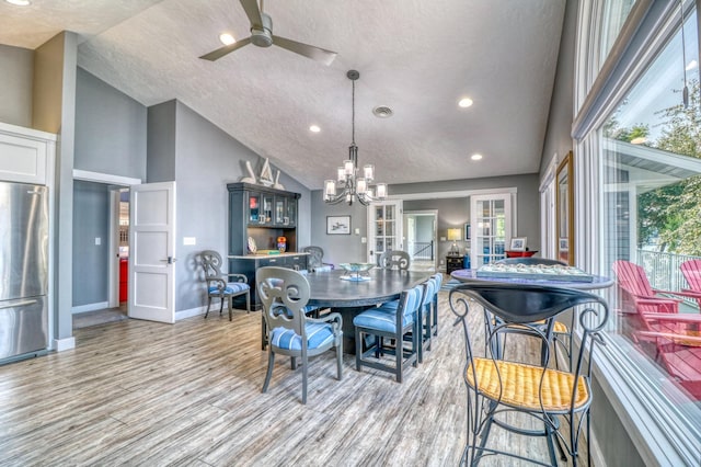 dining space featuring high vaulted ceiling, french doors, light wood-type flooring, a textured ceiling, and ceiling fan with notable chandelier