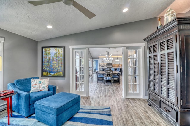 sitting room featuring french doors, light hardwood / wood-style floors, a textured ceiling, and lofted ceiling