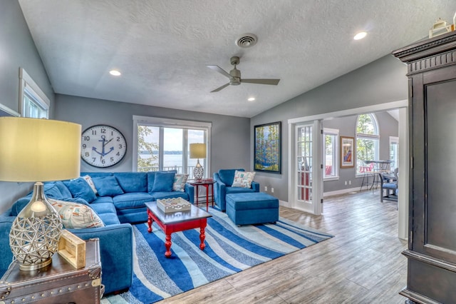 living room with ceiling fan, a textured ceiling, light wood-type flooring, vaulted ceiling, and baseboard heating