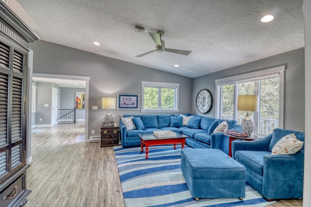 living room featuring lofted ceiling, light hardwood / wood-style flooring, a textured ceiling, and ceiling fan