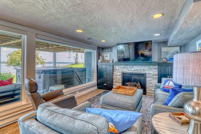 living room with a stone fireplace, a textured ceiling, and hardwood / wood-style floors