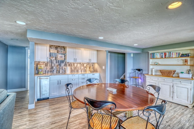 dining space featuring wine cooler, light hardwood / wood-style flooring, and a textured ceiling