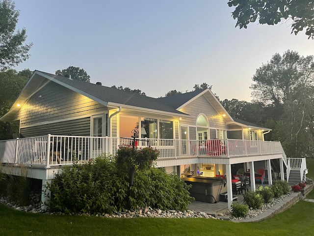 back house at dusk featuring a hot tub and a wooden deck