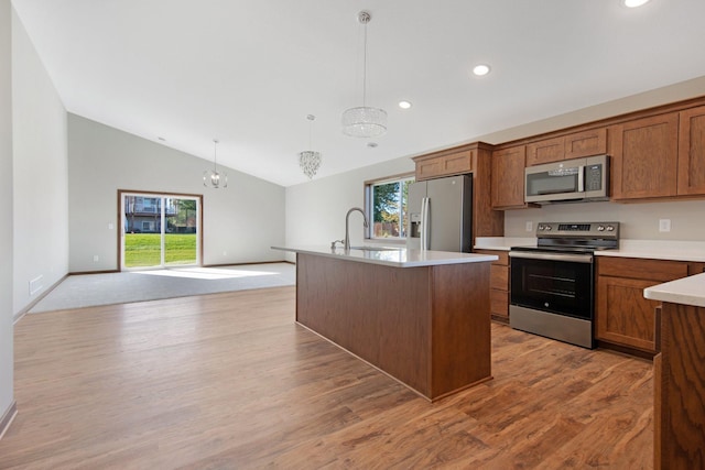 kitchen featuring appliances with stainless steel finishes, a kitchen island with sink, a chandelier, vaulted ceiling, and decorative light fixtures