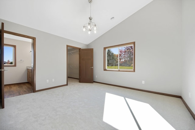 unfurnished bedroom with a walk in closet, a closet, high vaulted ceiling, an inviting chandelier, and light colored carpet