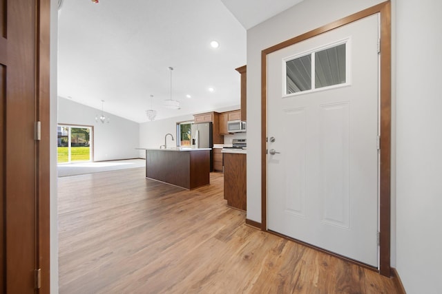 kitchen with a kitchen island with sink, light hardwood / wood-style flooring, vaulted ceiling, decorative light fixtures, and appliances with stainless steel finishes