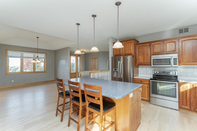 kitchen featuring a breakfast bar, tasteful backsplash, decorative light fixtures, a center island, and stainless steel appliances