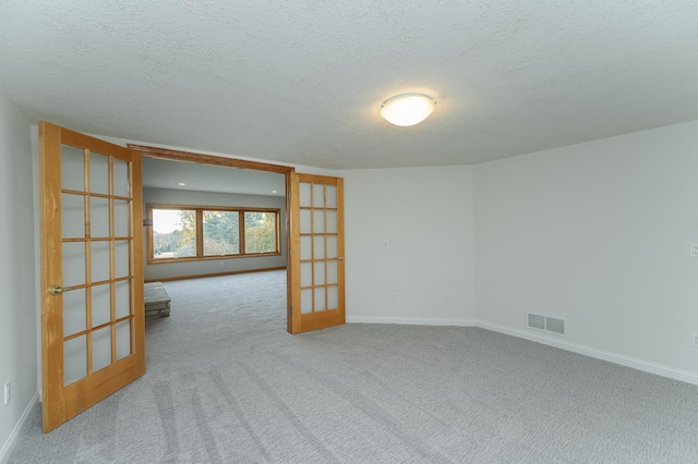 unfurnished room featuring light colored carpet, a textured ceiling, and french doors