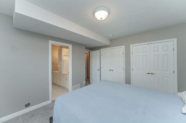 bedroom featuring light carpet, two closets, and ensuite bathroom