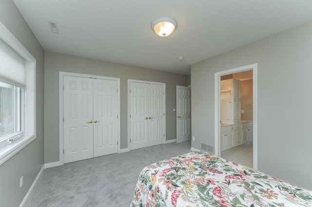 carpeted bedroom featuring connected bathroom and two closets