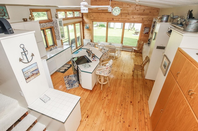 living room featuring ceiling fan, vaulted ceiling, light hardwood / wood-style flooring, wood walls, and sink