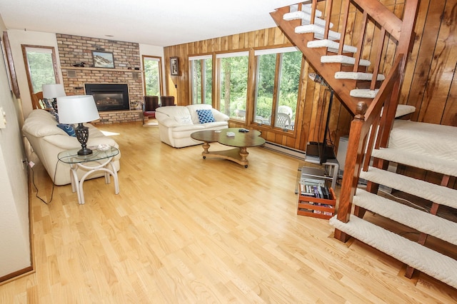 living room with light hardwood / wood-style floors, wood walls, baseboard heating, and a fireplace