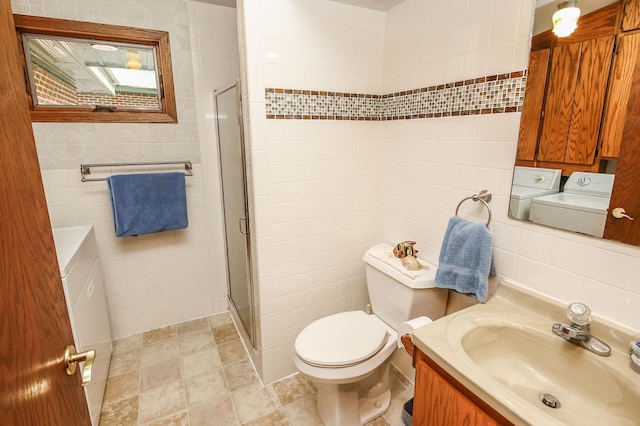 bathroom featuring toilet, vanity, tile walls, washer and dryer, and walk in shower