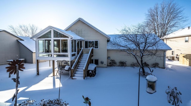 snow covered rear of property with a sunroom