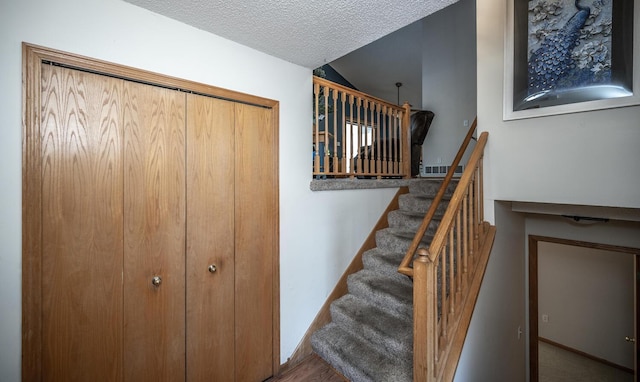 stairway with vaulted ceiling, hardwood / wood-style floors, and a textured ceiling