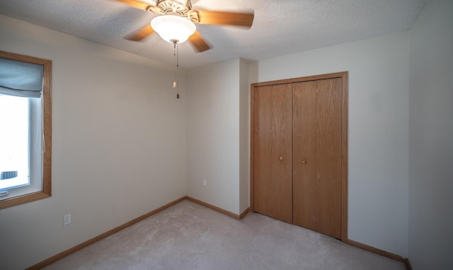 unfurnished bedroom with ceiling fan, light colored carpet, a textured ceiling, and a closet