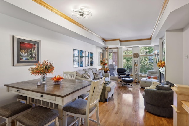 dining room with light hardwood / wood-style floors, a raised ceiling, and crown molding