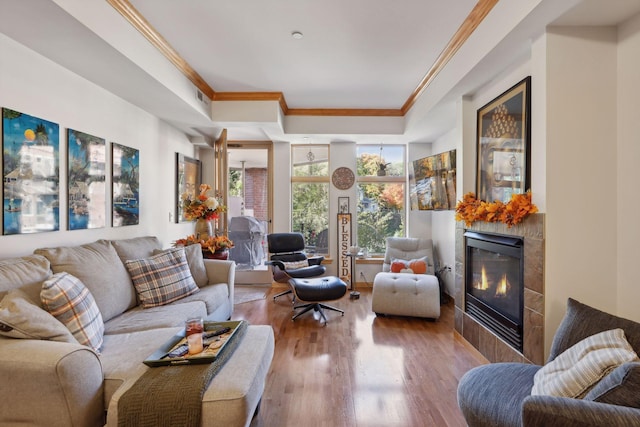 living room featuring a tiled fireplace, hardwood / wood-style flooring, and crown molding