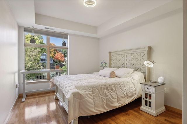 bedroom with hardwood / wood-style floors and a raised ceiling