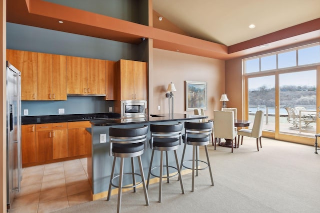 kitchen with appliances with stainless steel finishes, light tile patterned floors, high vaulted ceiling, an island with sink, and a breakfast bar area