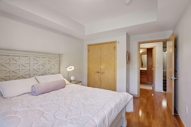 bedroom with a closet, baseboards, a tray ceiling, and wood finished floors