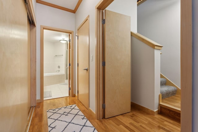 hallway featuring stairway, baseboards, crown molding, and light wood-style floors