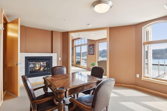 dining room with baseboards, a multi sided fireplace, and light carpet