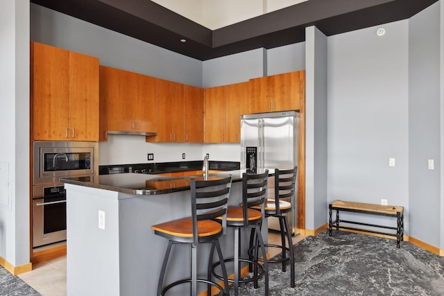 kitchen with a breakfast bar area, brown cabinetry, a kitchen island with sink, appliances with stainless steel finishes, and dark countertops