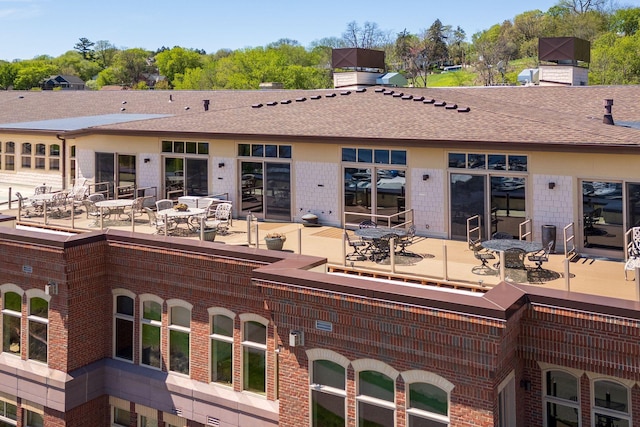 exterior space with outdoor dining space, brick siding, and a shingled roof