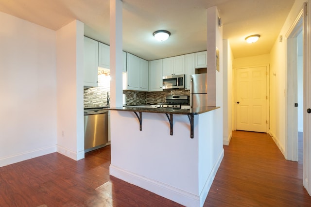 kitchen with a breakfast bar, white cabinets, decorative backsplash, appliances with stainless steel finishes, and dark hardwood / wood-style flooring